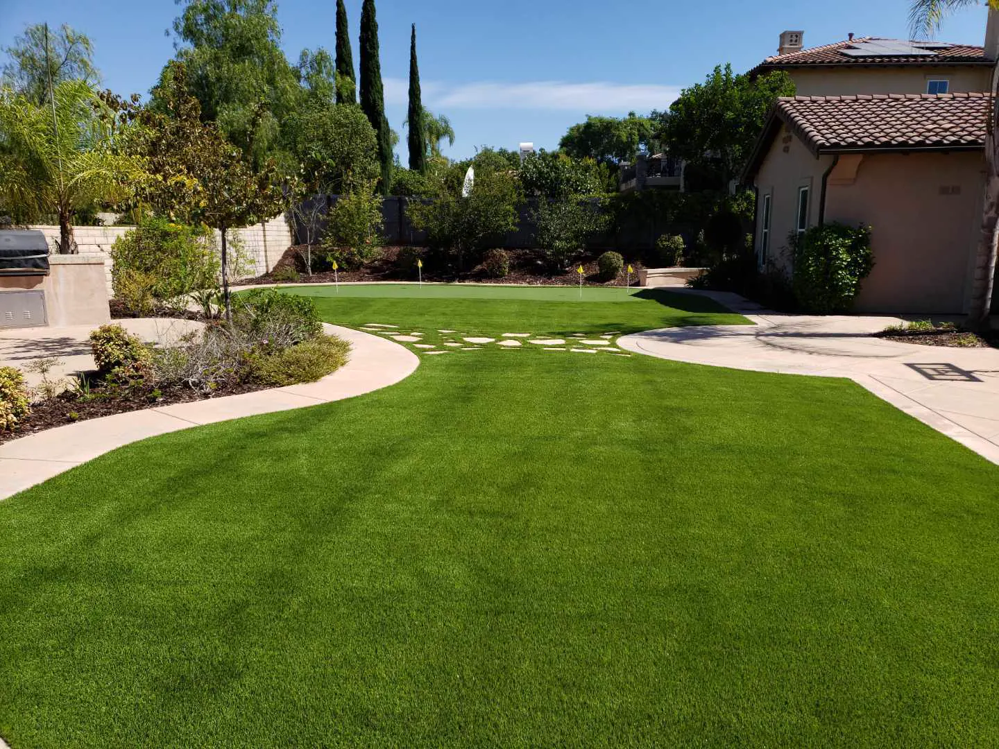 Same backyard after: green synthetic turf beside curved concrete paths