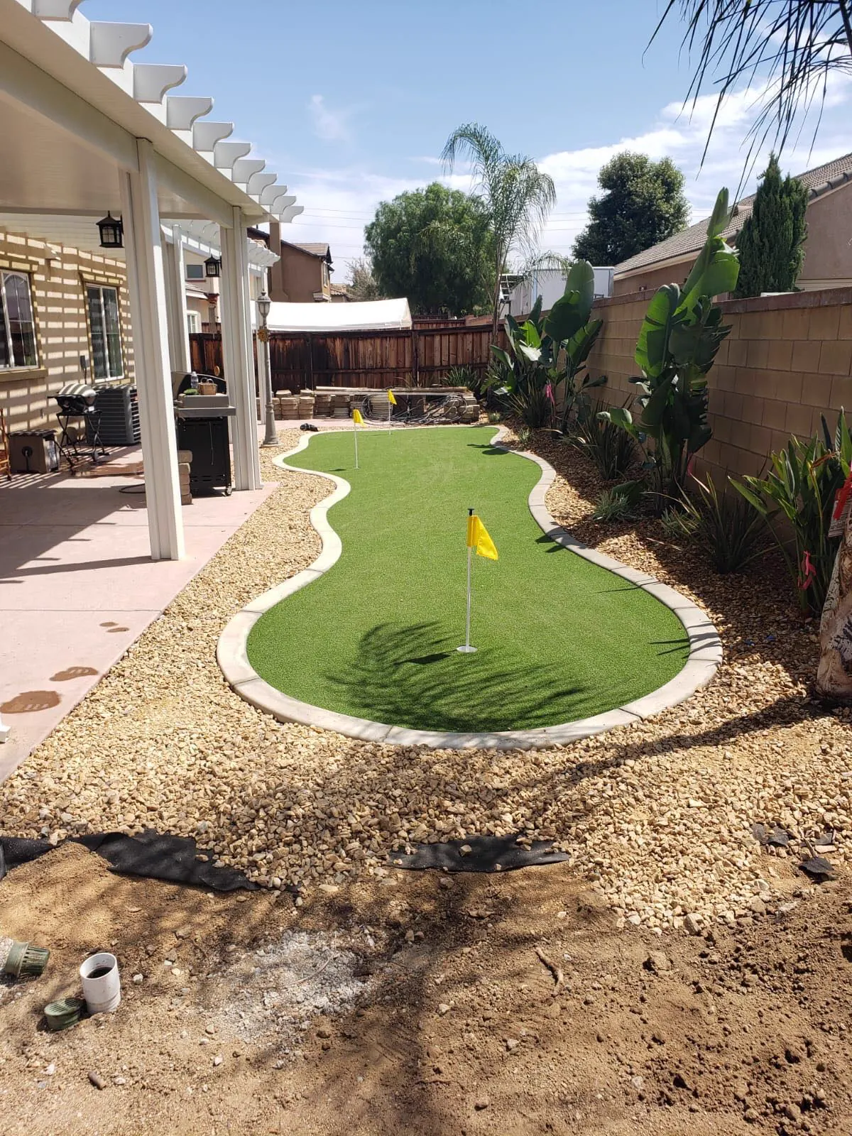 Side yard putting green with yellow flags, edged in concrete and surrounded by rock