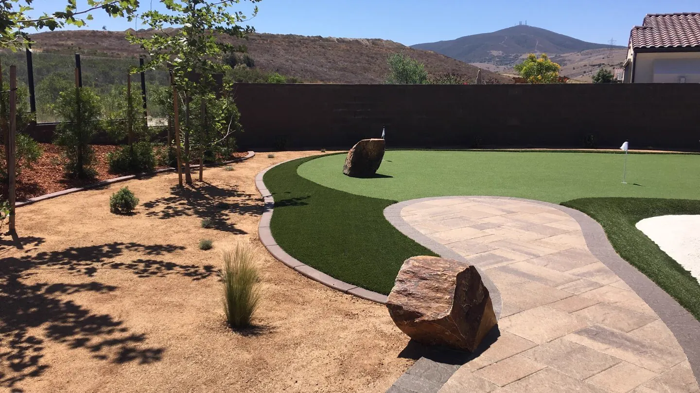 Mirage 94 putting green with boulders and a paver path in a desert backyard